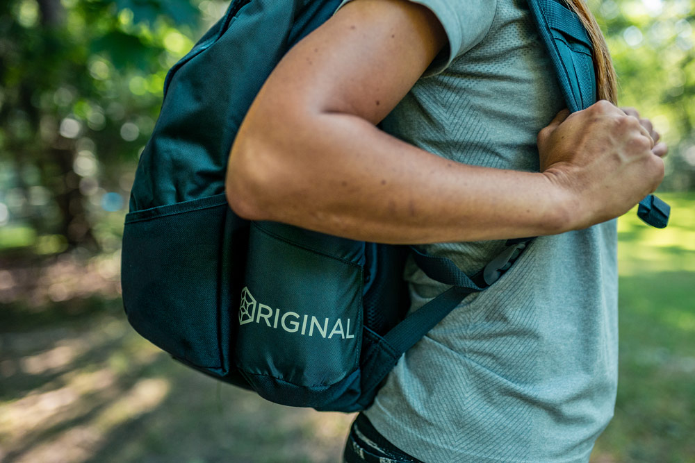 A side closeup view of a GRIPeq bag on someone's back, highlighting the word Original on the water bottle pocket.