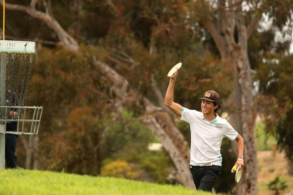 Anthony Barela walks towards the basket smiling and raising a disc in the air after putting.