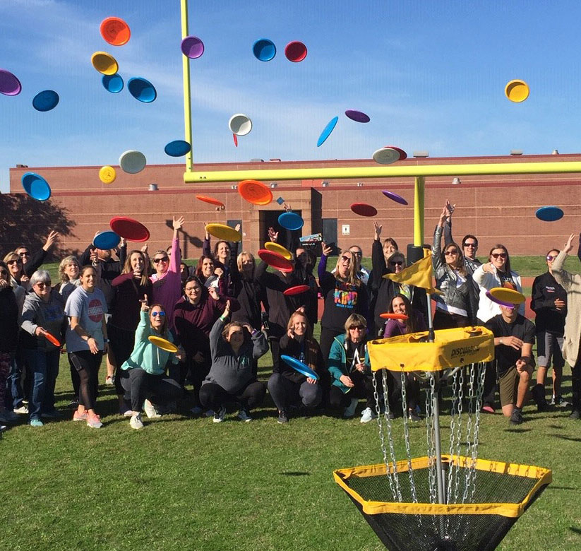 Many people at an EDGE disc golf event all throw discs into a disc golf basket at once.