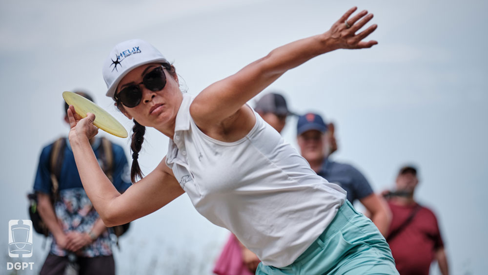 Team GRIPeq member, Ohn Scoggins, winds back to throw a forehand shot. Several spectators are in the background watching.