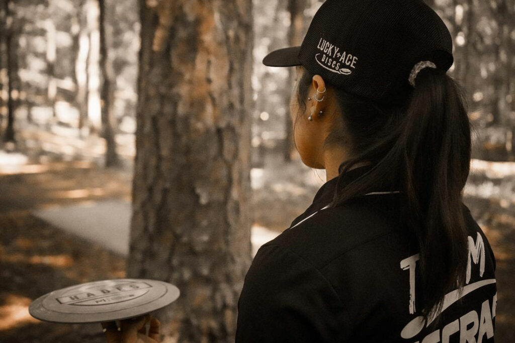 Alexis Mandujano, seen from behind her head, holding a disc in her hand and looking down the fairway.