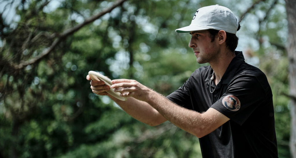 A side view of Silas Schultz holding a disc as he lines up a putt.