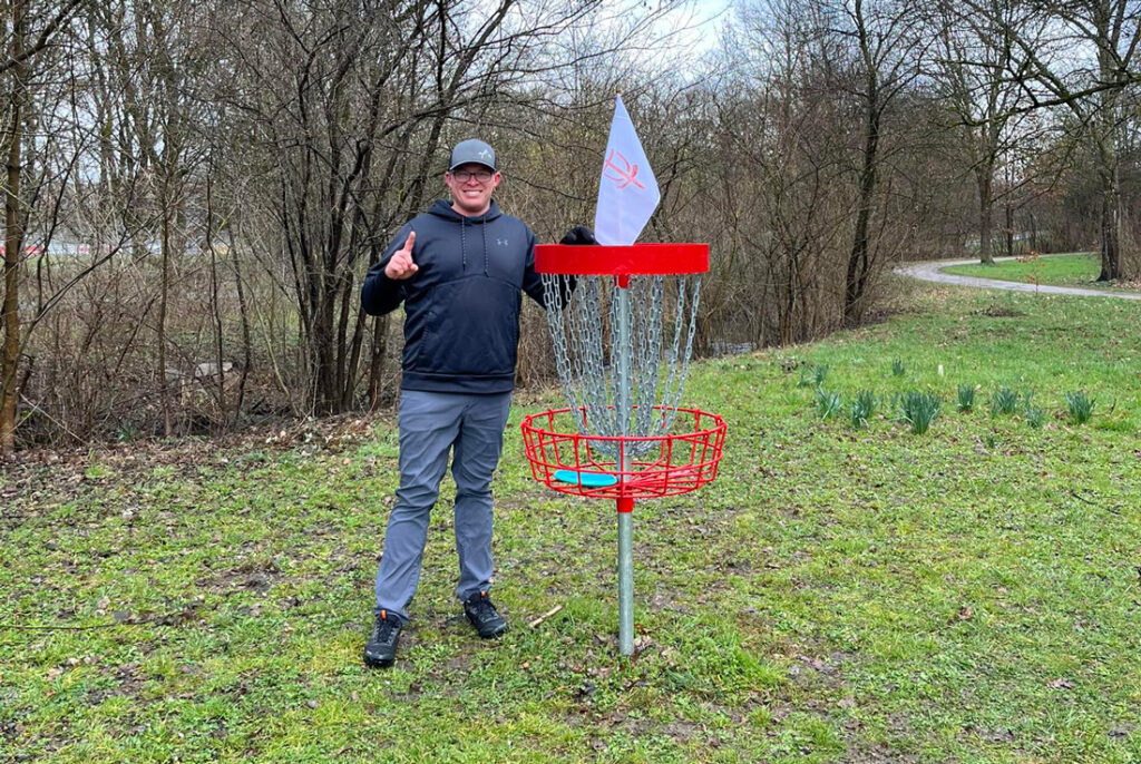 Team GRIPeq member Philip-Tyler Belt, standing next to a disc golf basket.