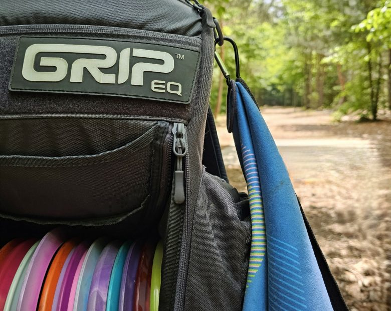GRIPeq Towel D Ring 2 One GRIPeq bag featuring a D Ring and a towel attached to the ring with a carabiner clip. There's a disc golf fairway in the background.